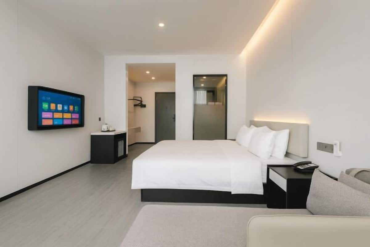 Une chambre d’hôtel moderne avec un grand lit, une table de chevet, un téléviseur fixé au mur et un petit bureau.