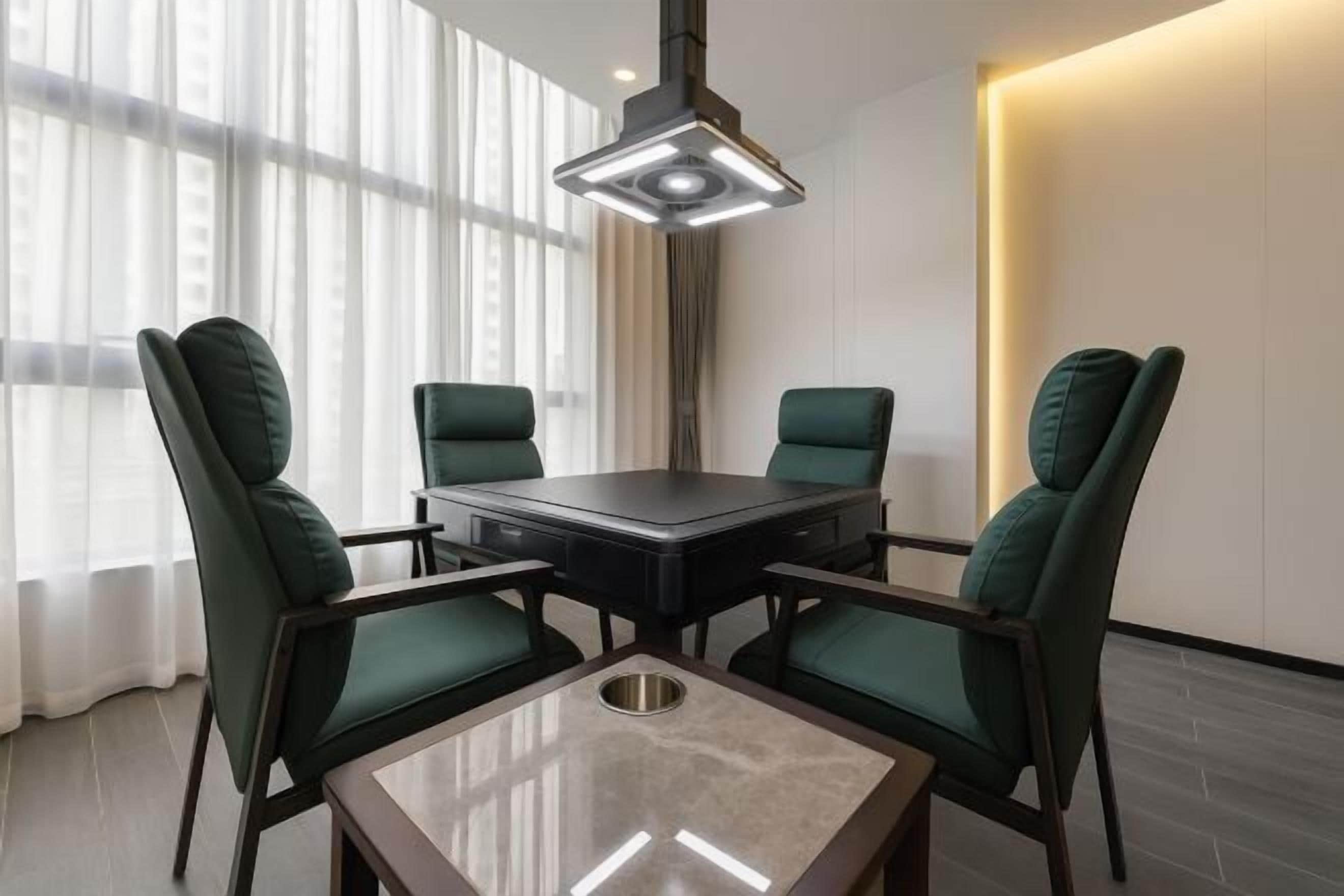 A conference room with a glass table, four dark green chairs, and a modern pendant light.