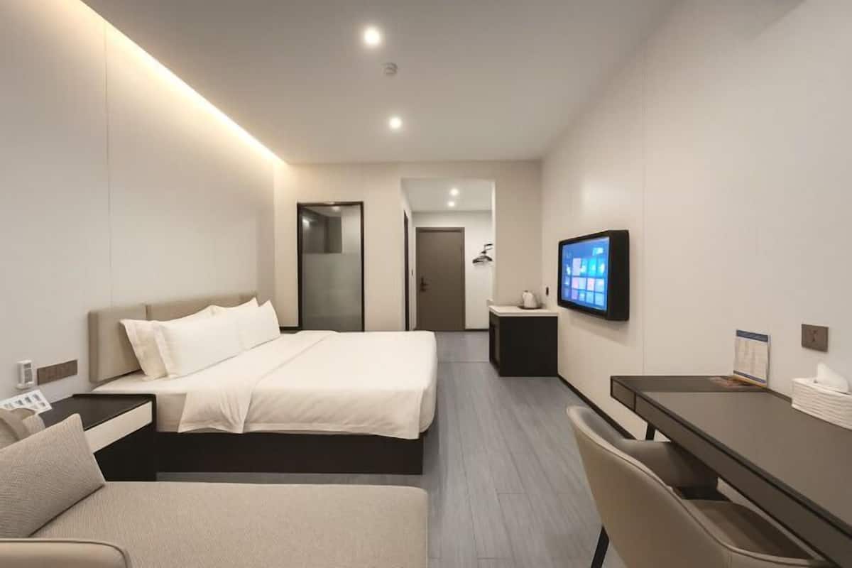 Une chambre d’hôtel moderne équipée d’un lit, d’un bureau, d’une chaise, d’une télévision et d’une petite table avec une lampe.