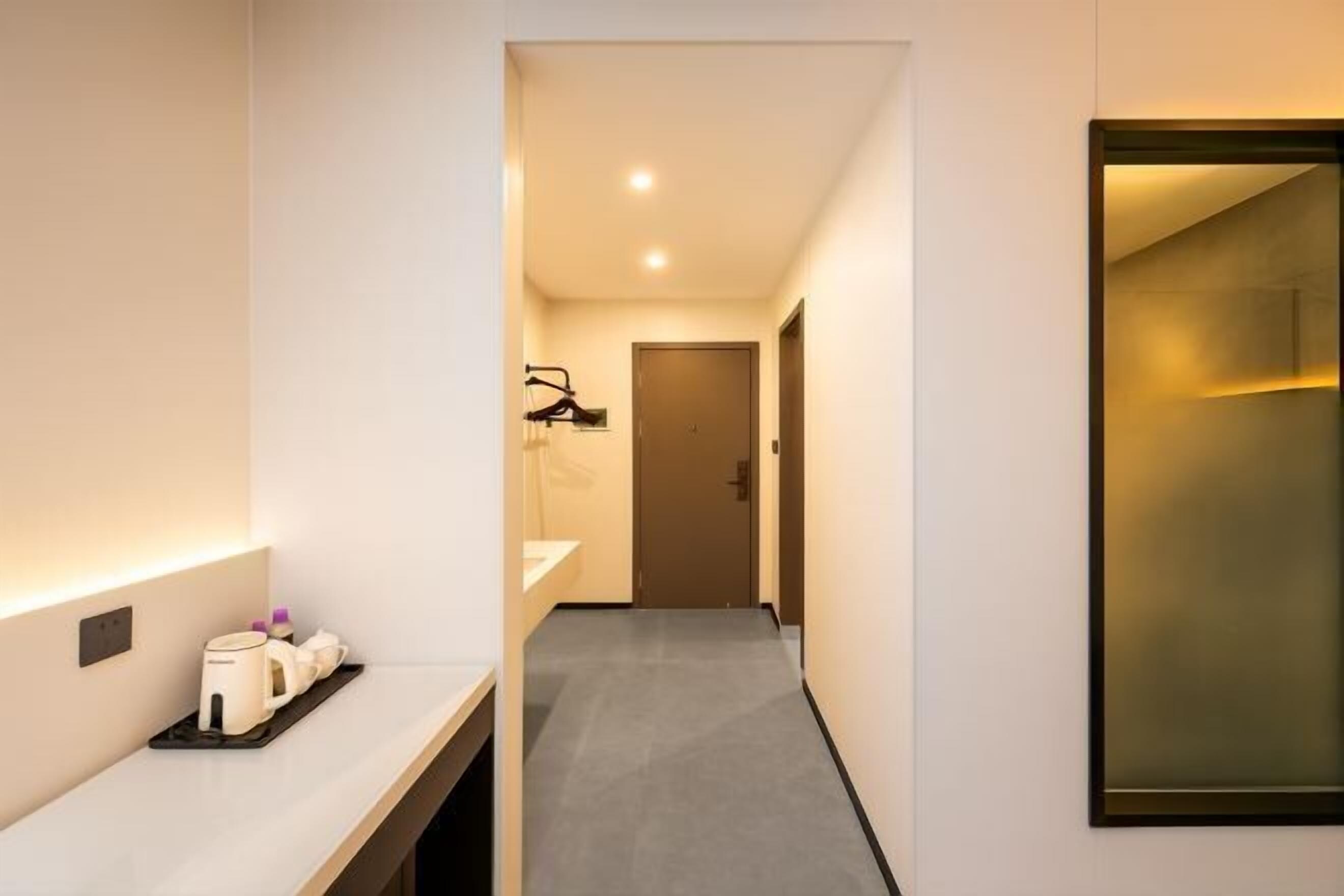 A modern hotel hallway with a minimalist design, featuring a long corridor, a reception area with a counter, and a door at the end.