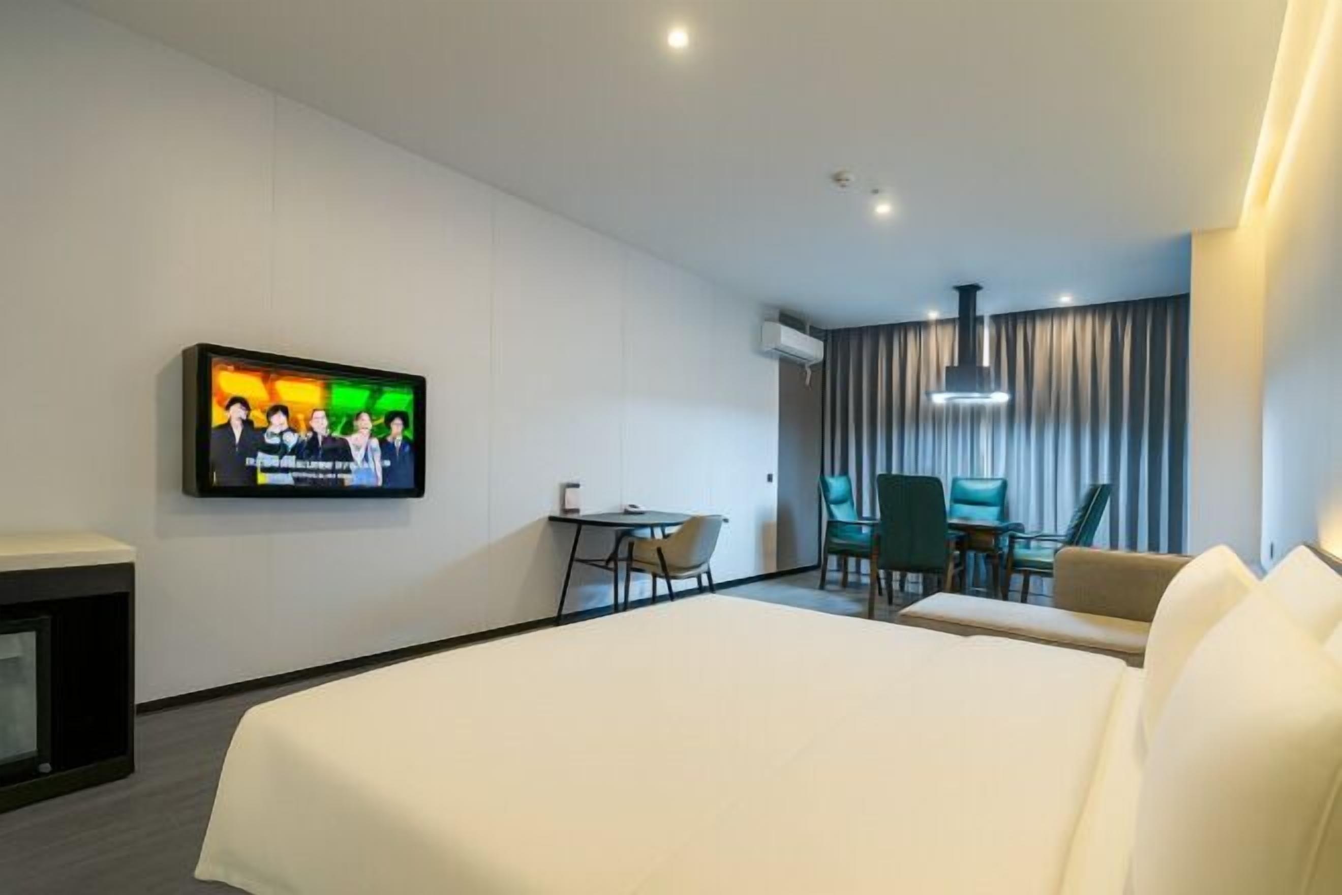 A hotel room with a bed, a TV mounted on the wall, a desk, and a chair.
