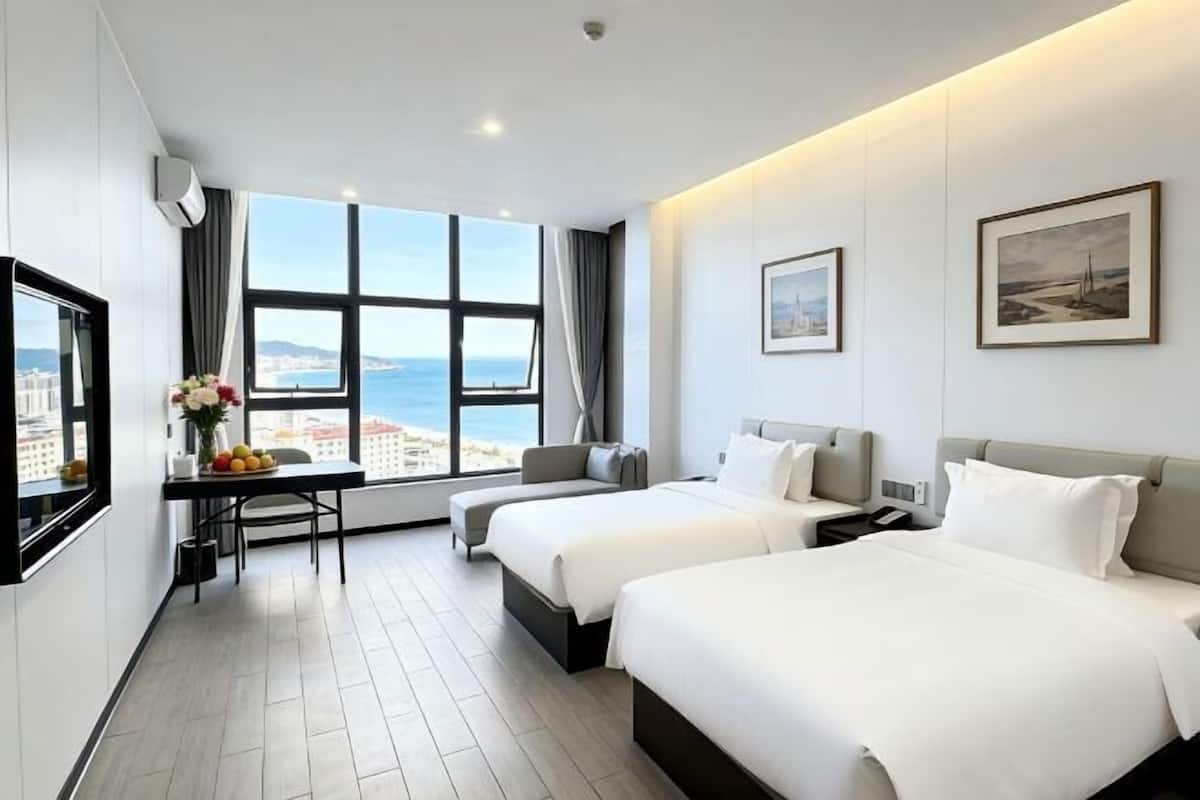 Une chambre d’hôtel avec deux lits, un bureau avec une chaise, une télévision et une grande fenêtre donnant sur la ville.