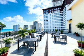 A rooftop terrace with outdoor seating, potted plants, and a view of the city skyline and ocean.