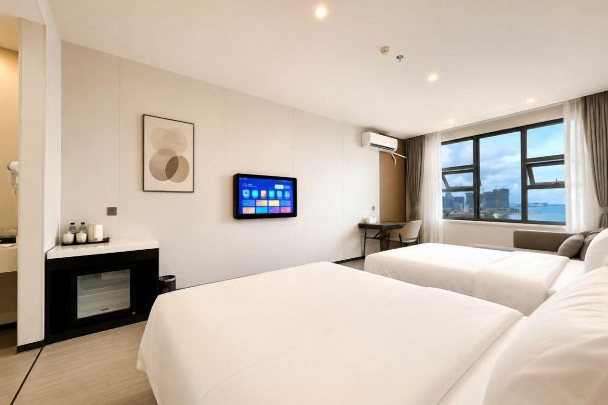 Een hotelkamer met twee bedden, een televisie, een bureau en een raam met uitzicht op de stad.