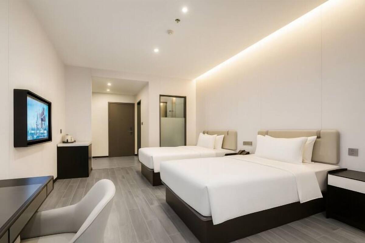 Une chambre d’hôtel moderne équipée de deux lits, d’un bureau, d’une chaise, d’une télévision et d’un miroir.