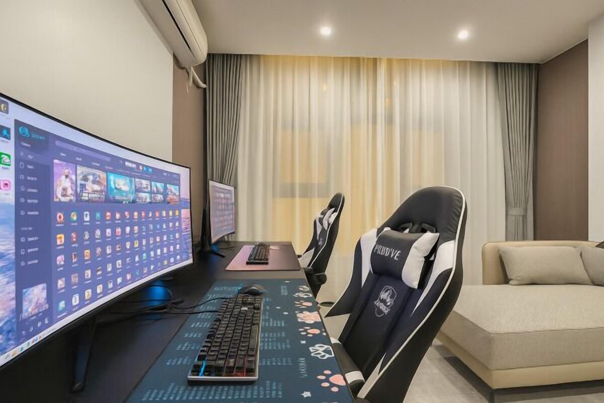 A gaming setup with a large monitor, keyboard, and gaming chair in a room with a sofa and curtains.