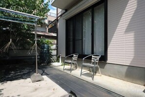 Une terrasse avec deux chaises, une balançoire suspendue et un bâtiment doté de grandes fenêtres.