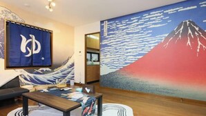 Ein Zimmer mit Tatami-Boden, einem niedrigen Holztisch, einer Couch und einem großen japanischen Gemälde vom Berg Fuji.