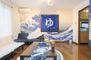 A living room with a traditional Japanese wave painting, a sofa, a coffee table, and a television. - Comfort Hasunuma (Tokyo)