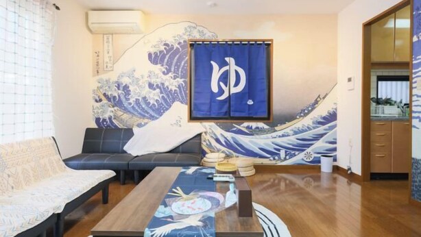 Ein traditioneller japanischer Raum mit Tatami-Bodenbelag, einem niedrigen Tisch mit Tischläufer, einer Couch und einem großen Wandgemälde mit dem Motiv einer Welle.