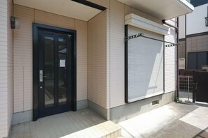 Une entrée d’immeuble avec une porte fermée, une fenêtre avec des stores et un sol carrelé.