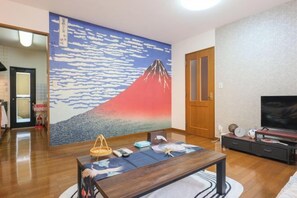 Una habitación con una obra de arte tradicional japonesa en la pared, una mesa de madera con una cesta tejida y un televisor sobre un pedestal.