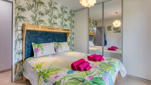 A bedroom with a bed, floral bedspread, a mirror, and a hanging light fixture.