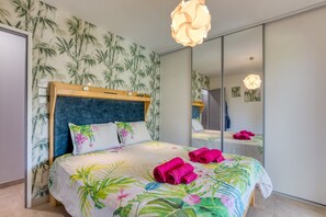Ein Schlafzimmer mit Bett, Spiegel und Wandgestaltung im tropischen Stil.