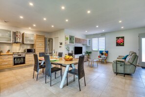 Une cuisine moderne dotée d’appareils électroménagers intégrés, un coin repas avec une table et des chaises, et un espace de vie avec un canapé et un téléviseur.