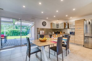 A modern kitchen with a dining area, large windows, and a view of the garden.