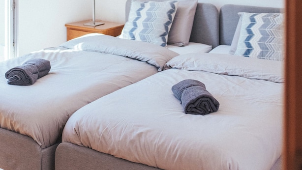 A bedroom with two beds, a nightstand, a lamp, and a beach-themed painting on the wall. - Baleal Paradise Inn (Peniche)