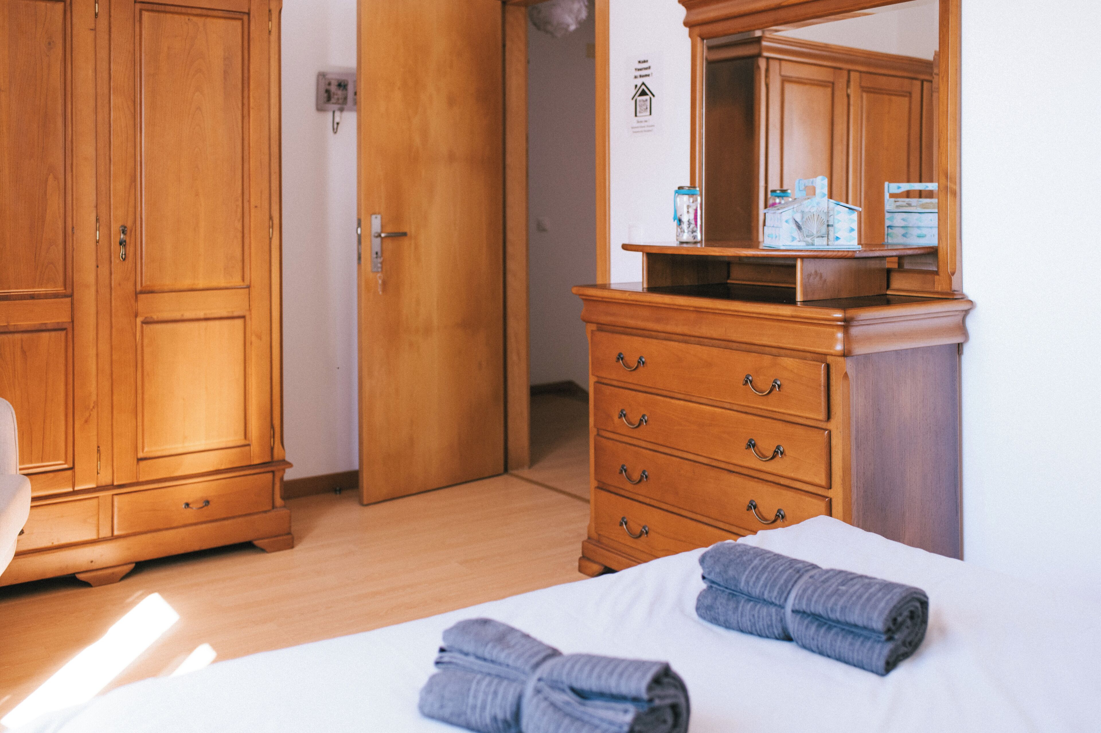 Ein Hotelzimmer mit einem Holzschrank, einem Schminktisch und einem Bett mit gerollten Handtüchern.