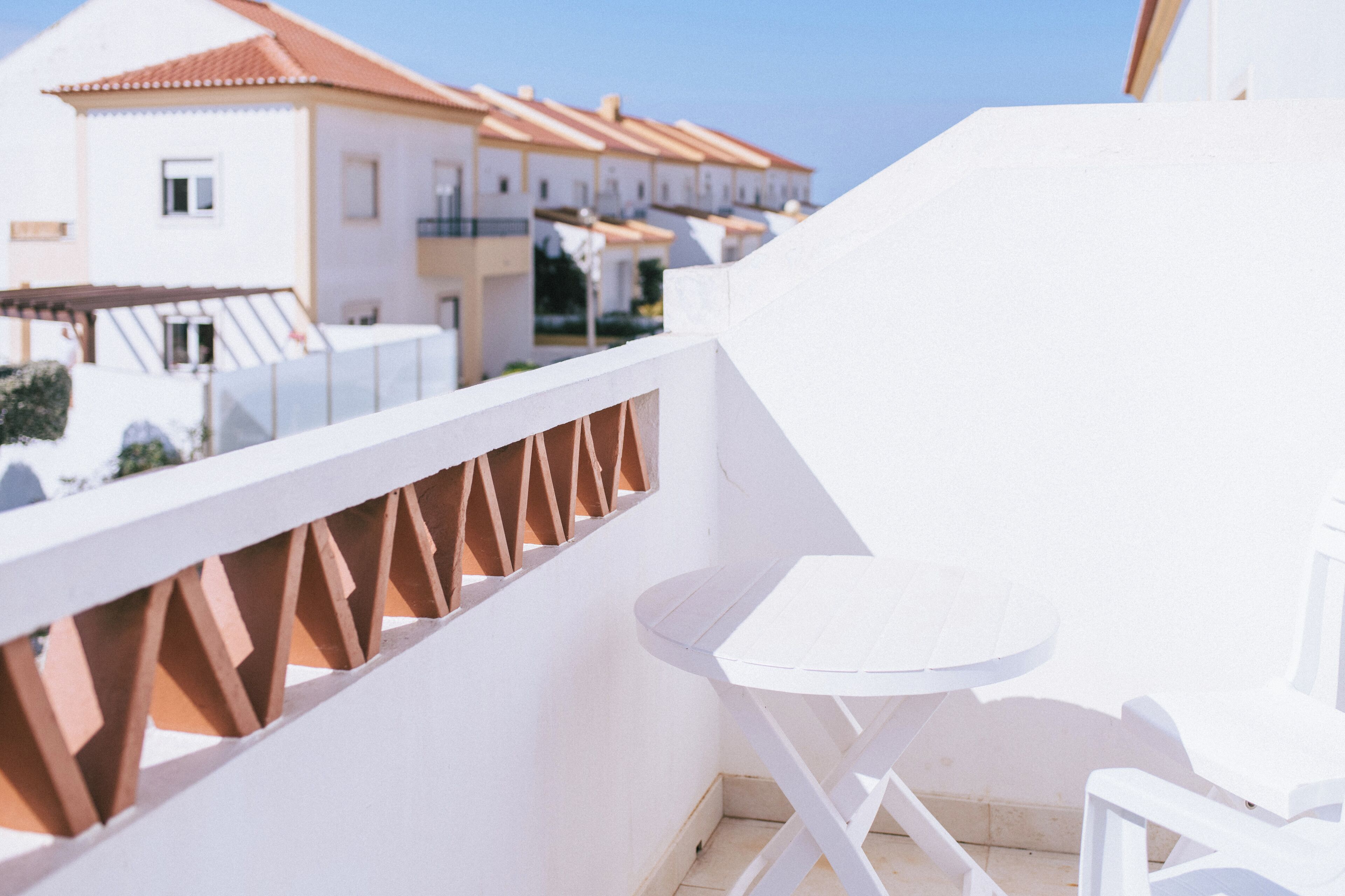 A balcony with a white table and chairs, a white railing, and a view of white buildings with red roofs.
