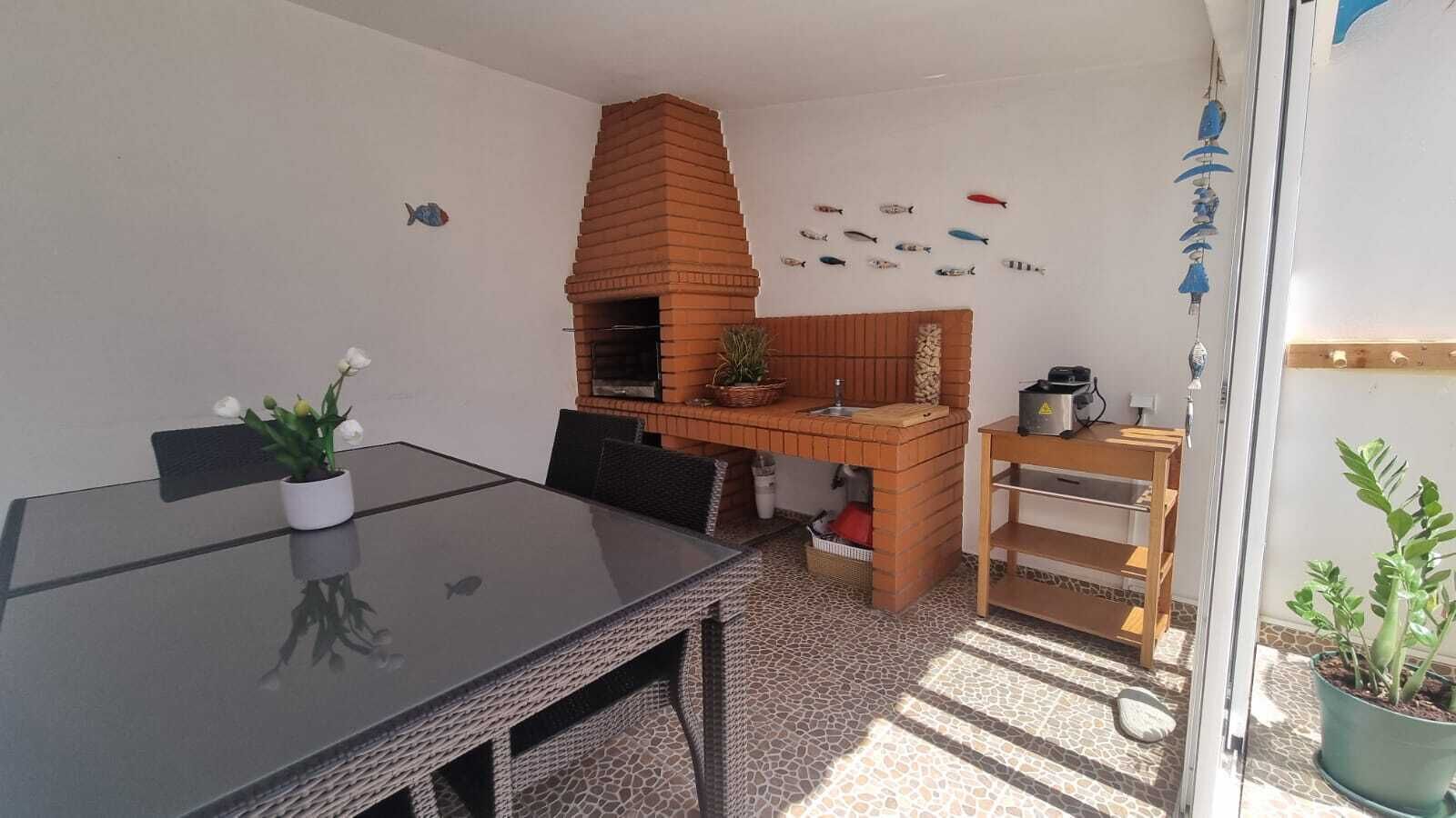 Un espace repas avec une table en verre, un four en briques et un petit coin cuisine comprenant une étagère et des plantes en pot.