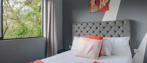 Un dormitorio moderno con cabecera capitonada, un ventanal con cortinas y un cuadro en la pared.