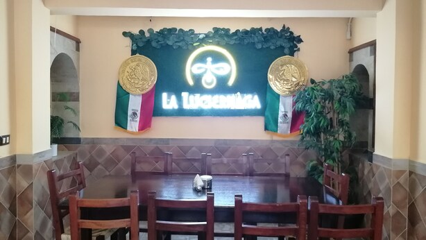 A restaurant with a large dining table, chairs, and a neon sign above. - Hotel San Fernando (Ciudad Valles)