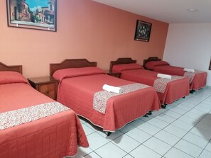 A hotel room with four beds arranged in a row, each with a red bedspread and a patterned pillow. There is a painting on the wall above the beds and a small nightstand with a lamp beside each bed. - Hotel San Fernando (Ciudad Valles)