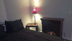 Une chambre à coucher avec un lit, une table de chevet, une lampe et une cheminée.