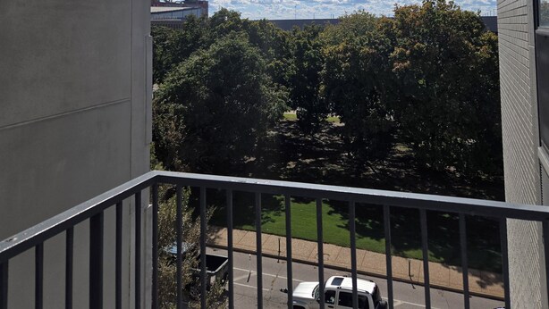 Un balcon donnant sur un parking et des arbres.