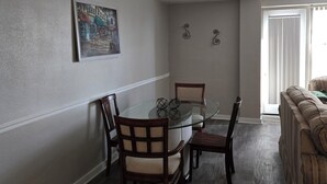 Un coin repas avec une table en verre et des chaises en bois, un tableau au mur et un canapé à l’arrière-plan.