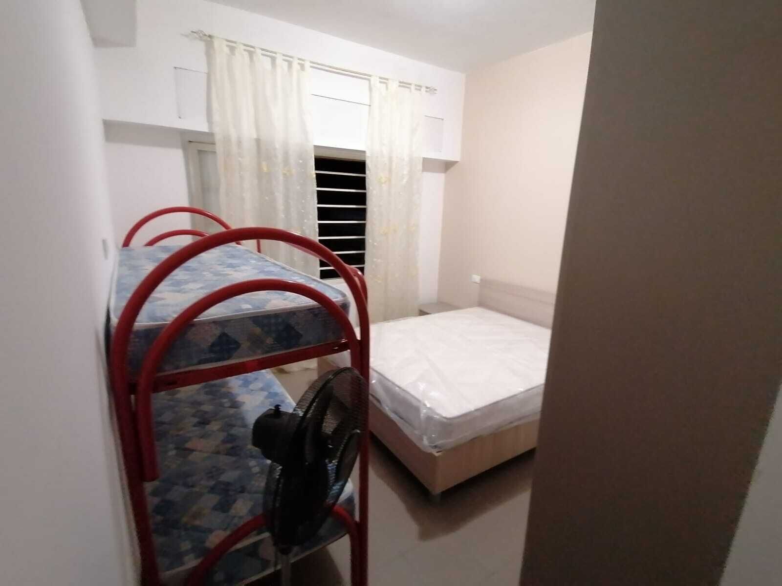 Una stanza piccola e compatta con letti a castello e un letto singolo. C'è una finestra con tende e un termosifone sopra i letti.