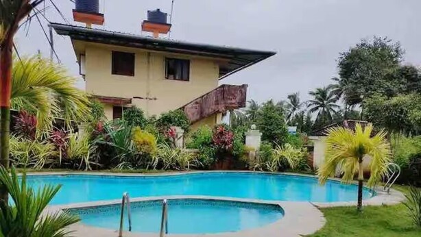 A swimming pool surrounded by lush greenery and a two-story building with a balcony. - Charming 3-bedroom apartment with AC in Goa, 500 mtrs from Zalor Beach, Goa (Goa)