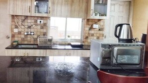 A kitchen with wooden cabinets, a black countertop, a kettle, and a microwave. - Charming 3-bedroom apartment with AC in Goa, 500 mtrs from Zalor Beach, Goa (Goa)