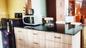 A modern kitchen with a black refrigerator, a white microwave, and a glass-top island with a kettle and a small plant. - Charming 3-bedroom apartment with AC in Goa, 500 mtrs from Zalor Beach, Goa (Goa)