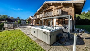 Una cabaña de madera con jacuzzi, mobiliario exterior y un camino de piedra.