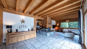 Un salón espacioso con chimenea de piedra, vigas de madera y un ventanal con vistas al verdor.