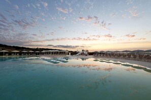 Une piscine entourée d’une clôture, avec des chaises longues et des parasols, sous un ciel dégagé.