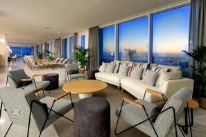 Un amplio vestíbulo de hotel con una gran zona de estar, un conjunto de sofás y vistas a la ciudad a través de amplias ventanas.