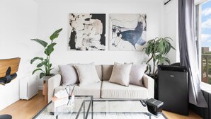 A modern living room with a sofa, two abstract paintings, a coffee table, a TV, and a plant. - Downtown Montreal Horizon W/ Balcony | 1BR Queen Bed, Sofa Bed, Parking & Gym (Montreal)