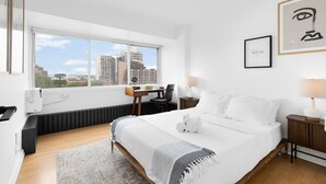 A modern hotel room with a large bed, a desk, and a view of the cityscape. - Downtown Montreal Horizon W/ Balcony | 1BR Queen Bed, Sofa Bed, Parking & Gym (Montreal)