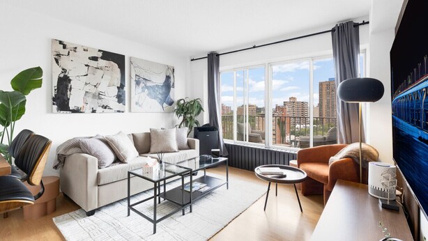A modern living room with a sofa, coffee table, and a TV. There are large windows with a city view. - Downtown Montreal Horizon W/ Balcony | 1BR Queen Bed, Sofa Bed, Parking & Gym (Montreal)
