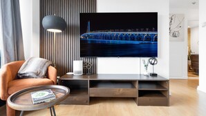A modern living room with a large flat-screen TV mounted on the wall, a comfortable armchair, a small round coffee table, and a minimalist entertainment unit. - Downtown Montreal Horizon W/ Balcony | 1BR Queen Bed, Sofa Bed, Parking & Gym (Montreal)