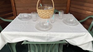 Ein Tisch ist gedeckt mit klarem Glas und einem Korbwannen, umgeben von grünen Stühlen, vor einem hölzernen Hintergrund.