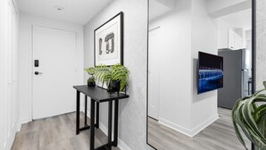 Een gang met een witte deur, een zwarte tafel met planten, een ingelijst beeld en een televisie aan de muur.