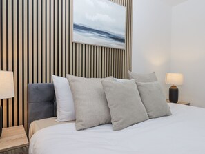Ein ordentlich eingerichtetes Hotelzimmer mit Bett, Kissen, Nachttisch, Lampe und Wandbild.