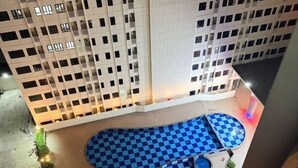 Une piscine sur le toit, avec un sol à motifs en damier, entourée d’un immeuble de grande hauteur doté de balcons.