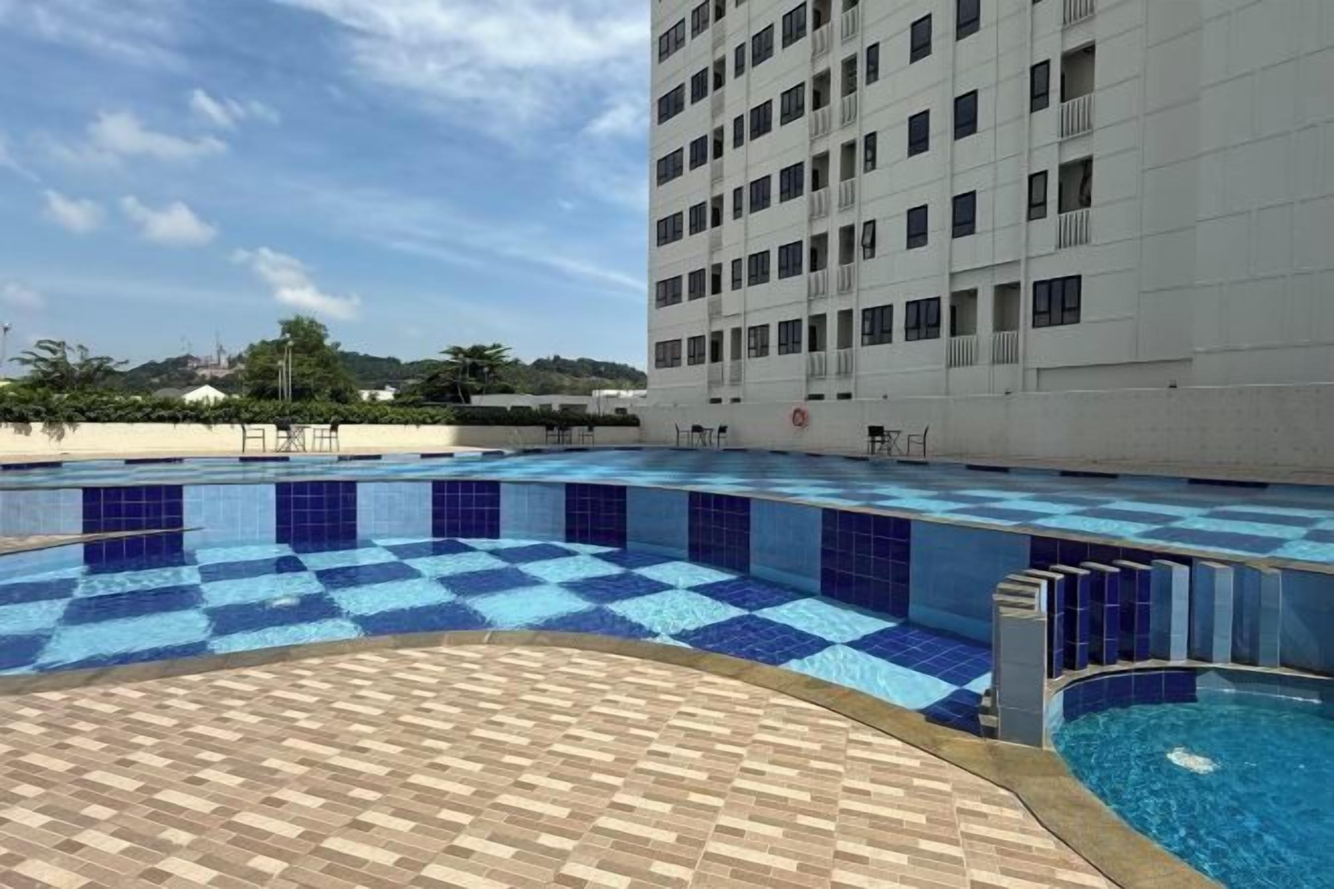 A swimming pool with blue tiles, a wooden deck, and a white building in the background.