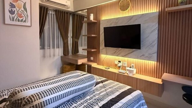 Une chambre à coucher moderne avec un grand lit, un téléviseur fixé au mur en bois et une petite table de chevet.