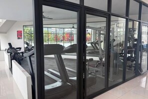 Une salle de sport équipée de matériel d’exercice, dotée de grandes fenêtres et offrant une vue sur l’extérieur.