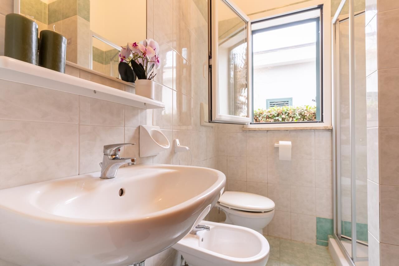 A bathroom with a large sink, toilet, and a window with a view of greenery.